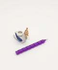 Small figurine with a purple candle-like object on a wooden surface