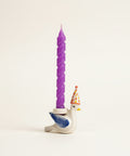 Purple twisted candle on a small figurine of a duck with a birthday hat on a desk.
