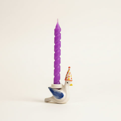 Purple twisted candle on a small figurine of a duck with a birthday hat on a desk.