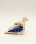 Decorative ceramic dove figurine on a wooden surface with a laptop in the background.