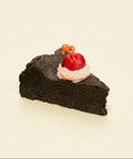 Slice of chocolate cake with a cherry on top on a wooden table