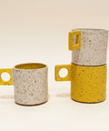Two ceramic mugs with speckled texture and yellow accents on a wooden surface.