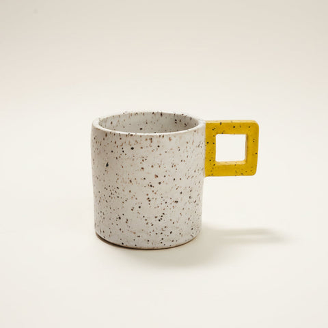 Speckled mug with a yellow handle on a wooden surface