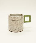 Speckled mug with a green handle on a wooden surface