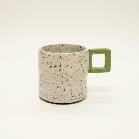 Speckled mug with a green handle on a wooden surface