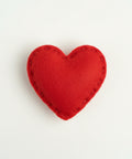 Red heart-shaped catnip toy in clear packaging with a label on a textured fabric background