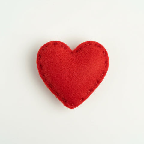 Red heart-shaped catnip toy in clear packaging with a label on a textured fabric background
