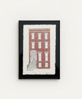 Framed artwork of a red brick building on a wooden surface