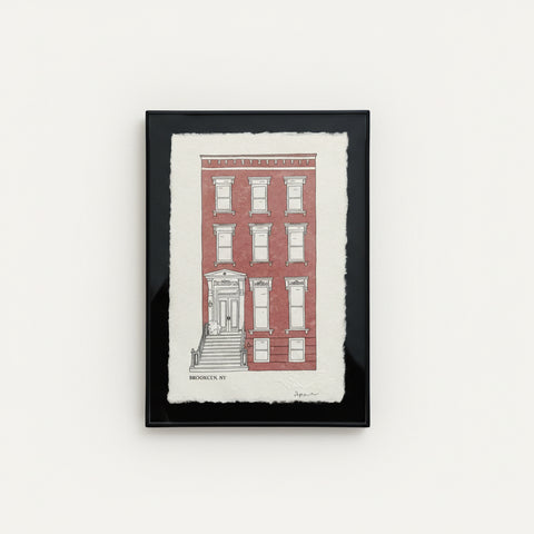 Framed artwork of a red brick building on a wooden surface