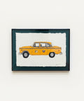 Framed artwork of a yellow taxi on a wooden floor