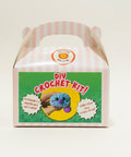 DIY crochet kit packaging on a wooden surface with a blurred background