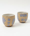 Two ceramic cups with gray patterns on a wooden surface, with a blurred background.