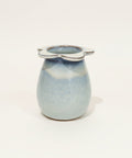 Small ceramic jar with a blue glaze and white handle on a light gray background