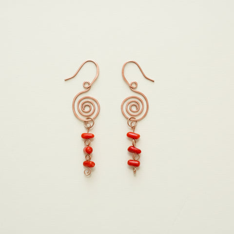 Copper spiral earrings with red beads on a wooden surface