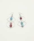 Pair of earrings with geometric designs and colorful beads on a wooden surface