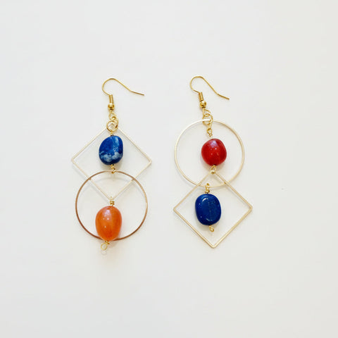 Gold earrings with blue and orange stones on a wooden surface
