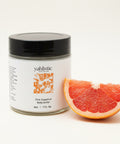 Jar of yahlistic Pink Grapefruit Body Butter on a wooden surface with an Apple product in the background.