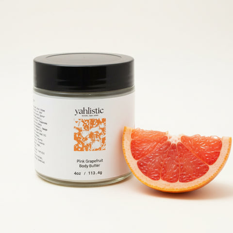 Jar of yahlistic Pink Grapefruit Body Butter on a wooden surface with an Apple product in the background.