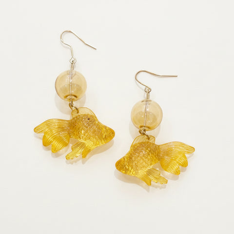 Gold fish-shaped earrings with clear beads on a wooden surface
