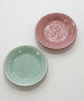 Two ceramic plates, one pink and one green, on a wooden surface.