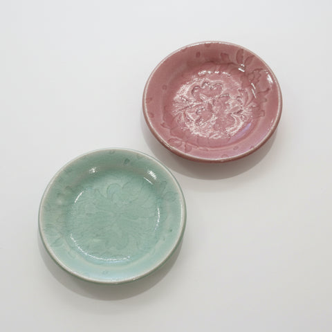 Two ceramic plates, one pink and one green, on a wooden surface.