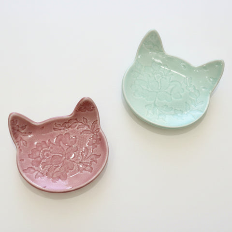 Two ceramic cat-shaped dishes, one pink and one green, on a wooden surface.