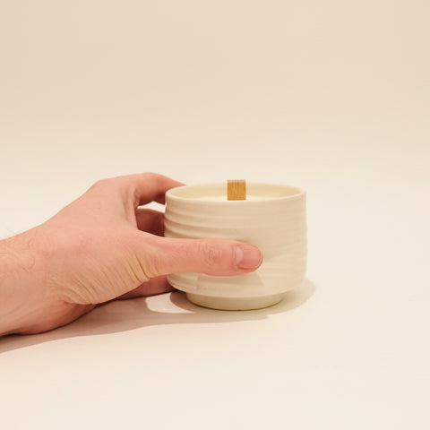 Hand holding a small white ceramic container on a wooden surface with a blurred background