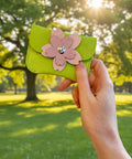 Hand holding a green cardholder with a pink flower design in a park.