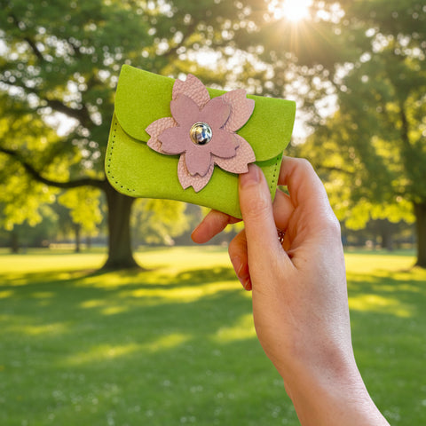 Hand holding a green cardholder with a pink flower design in a park.