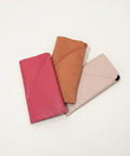 Three phone cases in pink, brown, and beige on a wooden surface.