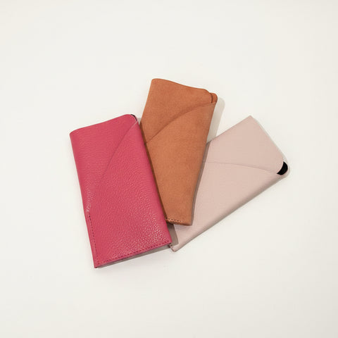 Three phone cases in pink, brown, and beige on a wooden surface.