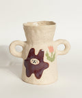 Ceramic vase with handles and decorative elements on a wooden surface.