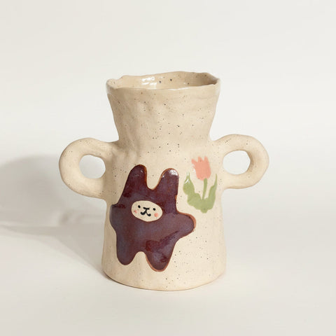Ceramic vase with handles and decorative elements on a wooden surface.