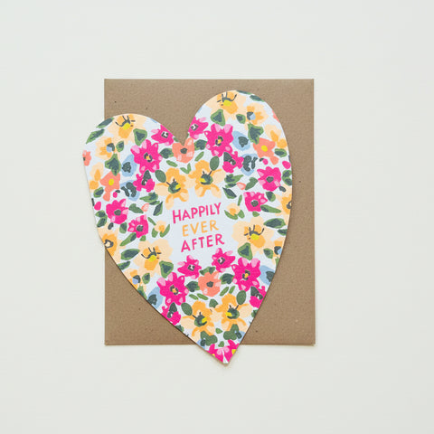 Heart-shaped card with floral design and 'Happily Ever After' text on a wooden surface