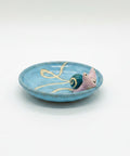 Ceramic snail on a blue plate on a wooden table with a laptop and snacks in the background.