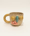 Speckled ceramic mug with face-like design on a wooden surface, Apple laptop in the background.