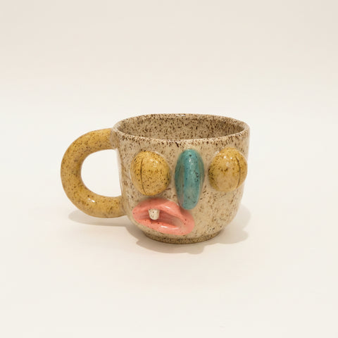 Speckled ceramic mug with face-like design on a wooden surface, Apple laptop in the background.