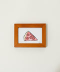 Framed drawing of a slice of pizza on a wooden surface