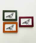 Three framed illustrations of pigeons on a wooden surface