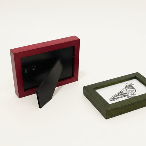Two picture frames on a wooden surface, one red and one black with a design.