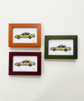 Three framed illustrations of yellow taxis on a wooden surface