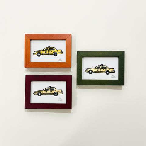 Three framed illustrations of yellow taxis on a wooden surface