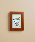 Small framed drawing of a cocktail on a wooden surface