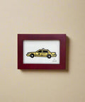 Framed artwork of a yellow taxi on a wooden surface