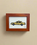 Small framed picture of a yellow taxi on a wooden surface