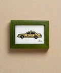 Framed drawing of a yellow taxi on a wooden surface