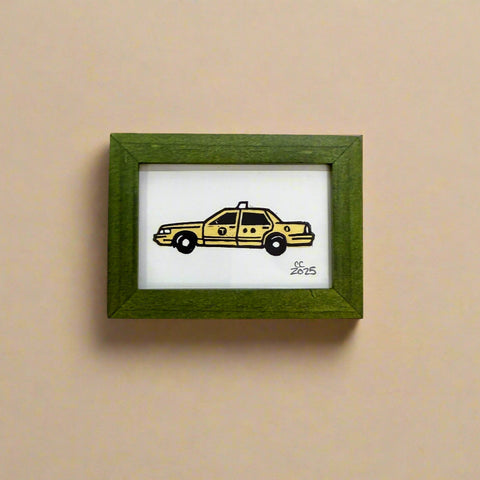 Framed drawing of a yellow taxi on a wooden surface