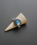 Ring with a blue gemstone on a beige cone-shaped object against a wooden background
