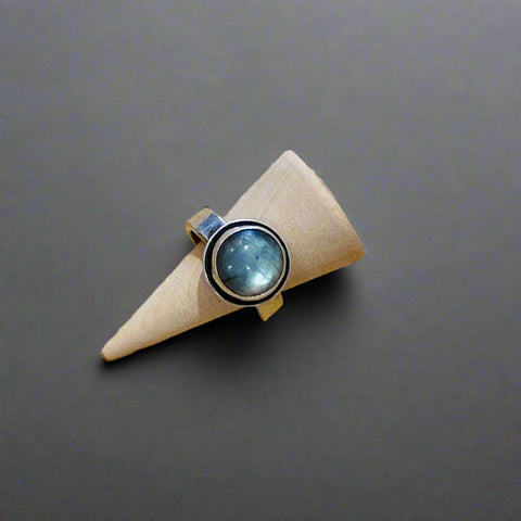 Ring with a blue gemstone on a beige cone-shaped object against a wooden background