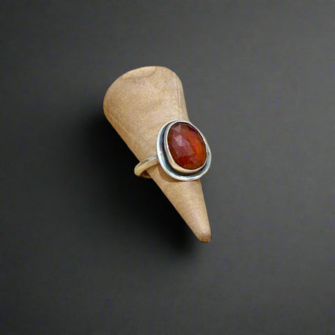 Silver ring with a red stone on a beige cone against a wooden background